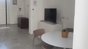 A modern, minimalist living room with a round table, two chairs, a flat-screen TV, and a small potted plant. - Detached house near the sea (Livorno)