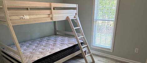 A bunk bed room with a ceiling fan, a window with blinds, and a wooden floor.