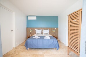 A hotel room with a bed, two bedside tables, a wooden headboard, and a wall-mounted air conditioner.