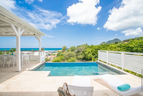 Une piscine avec vue sur l’océan, un patio couvert et des chaises longues.