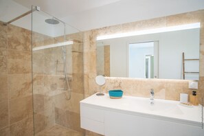 A modern bathroom with a glass-enclosed shower, a white vanity with a mirror, and beige tiles.