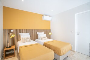 A hotel room with two beds, each with a headboard, a bedside table, and a lamp.