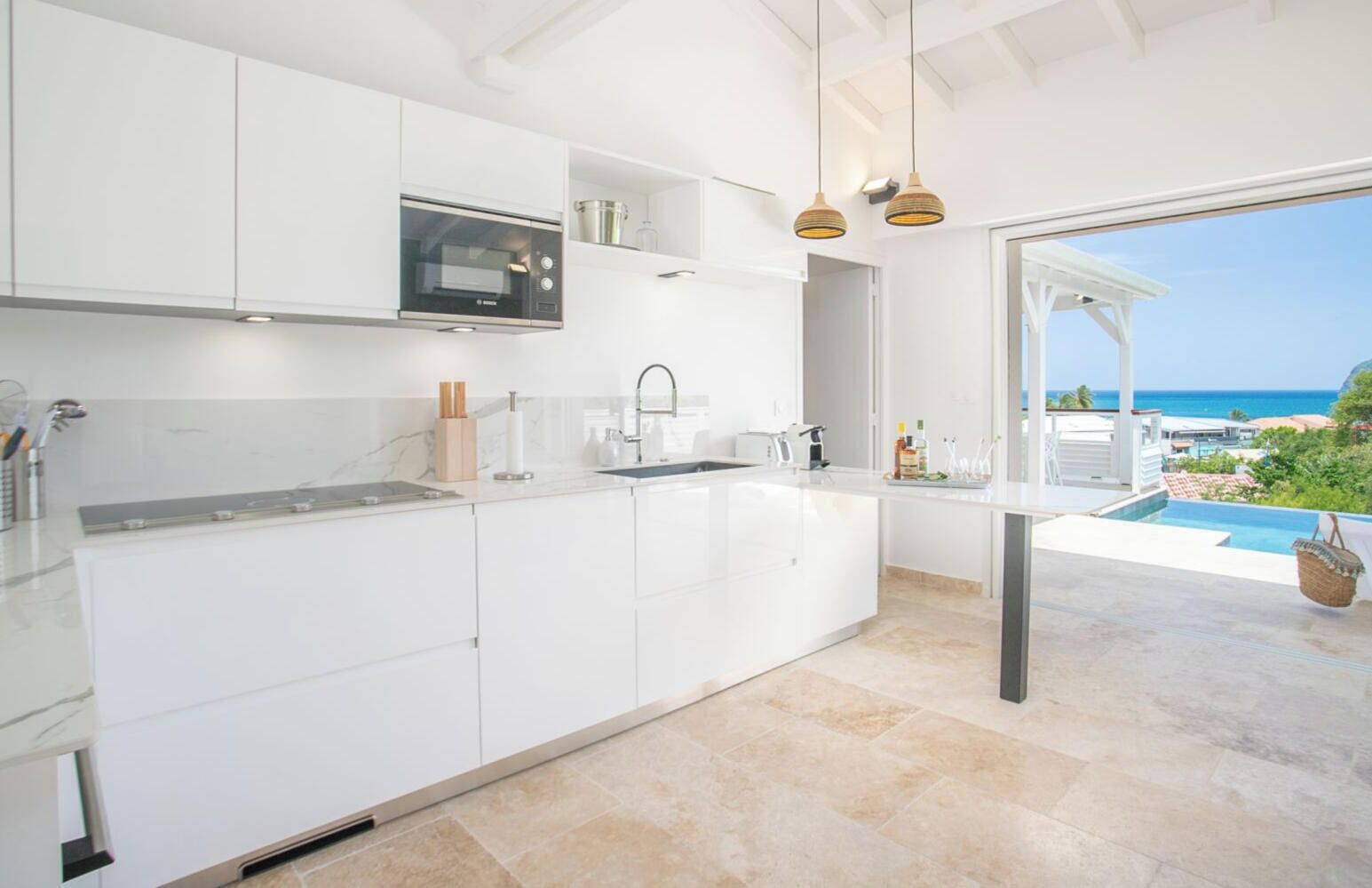 A modern kitchen with white cabinetry, a built-in oven, and a view of a pool and ocean.