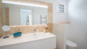 Une salle de bain avec un lavabo blanc, un miroir rond, un panier bleu, une échelle en bois et des toilettes blanches.