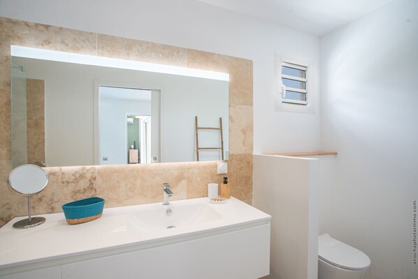 A bathroom with a white sink, a round mirror, a blue basket, a wooden ladder, and a white toilet.