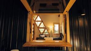 Ett mysigt rum med ett träpanelat tak, ett fönster med en triangulär form, en soffa och en lampa.