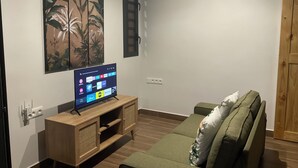 A living room with a flat-screen TV on a wooden stand, a green sofa, and a wall-mounted painting. - Charming bungalow in peaceful property with WiFi, AC in Fare, Huahine (Huahine)