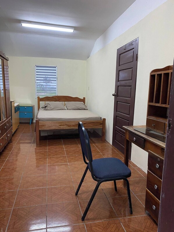 A small, well-lit bedroom with a bed, a desk, and a chair.