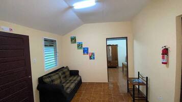 A room with a brown tiled floor, a black sofa, a wooden cabinet, and a small table.