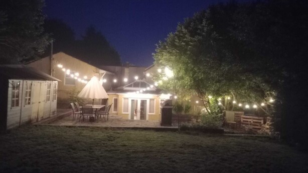 Een terras buiten met lichtjes, een tafel, stoelen en een overdekte zithoek.