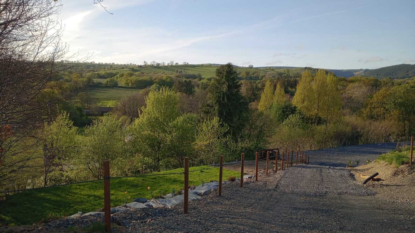 A rural landscape with a gravel path, trees, and a fence.