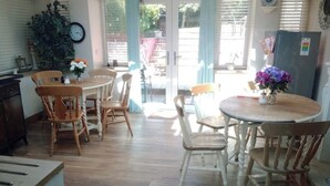 Een eetgedeelte met houten stoelen en een ronde tafel, een kamerplant en een klok aan de muur.