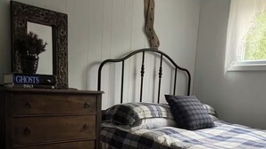 Een slaapkamer met een bed, een dressoir, een spiegel en een raam.