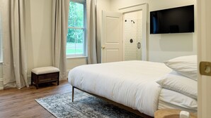A bedroom with a bed, a TV mounted on the wall, a shower area, and a window with curtains. - Historical Charm-Saugatuck City-Sleeps 8 (Saugatuck)