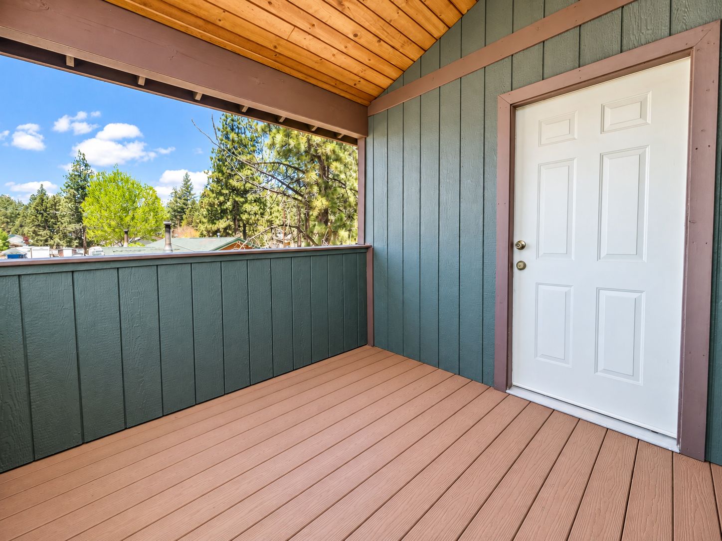 Un porche couvert avec un plancher en bois et une porte blanche.