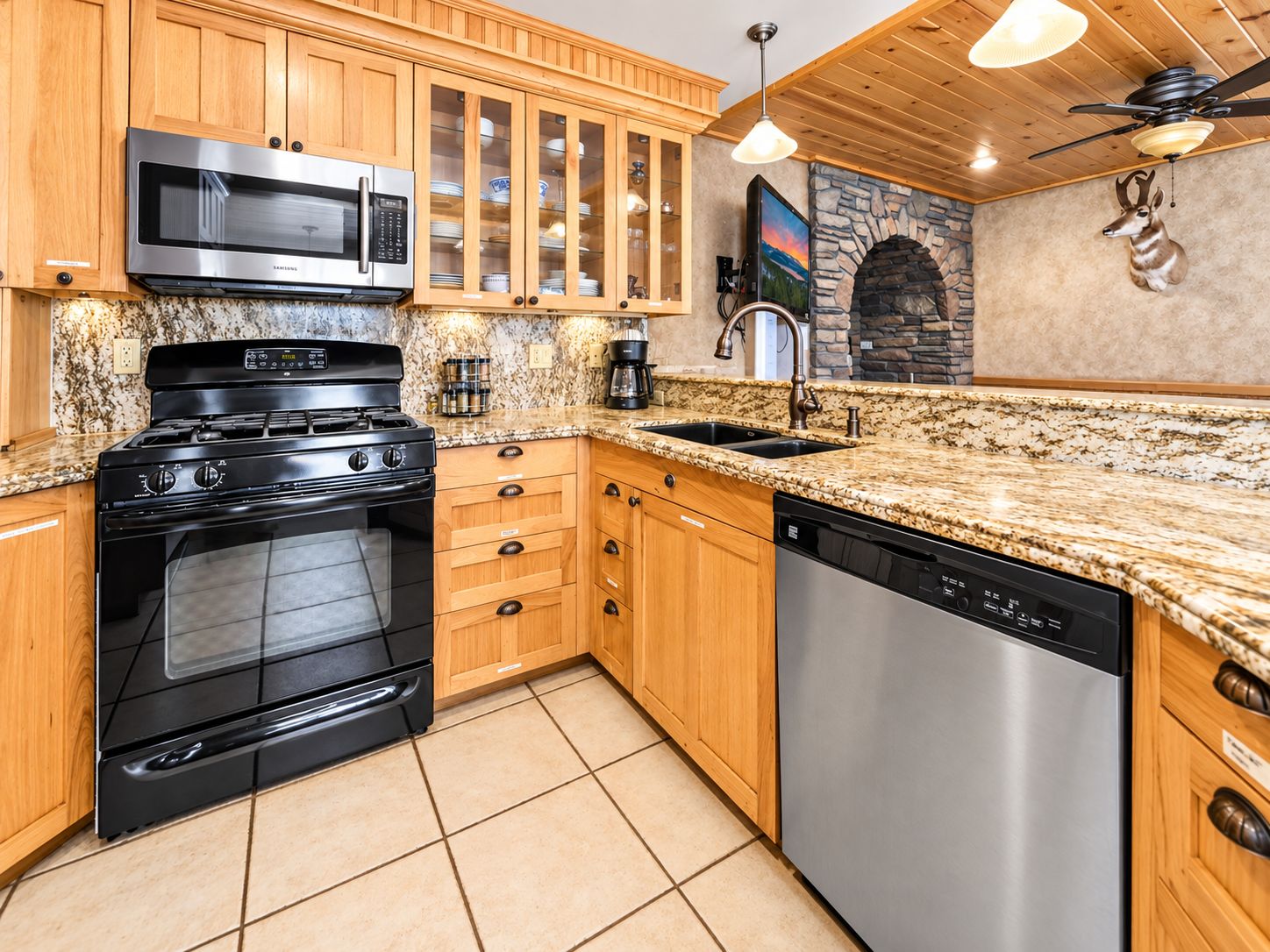 A kitchen with wooden cabinets, a stainless steel microwave, a gas stove, a dishwasher, and a stone fireplace.