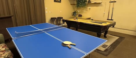 Una habitación con mesa de ping pong azul, mesa de billar y billar.