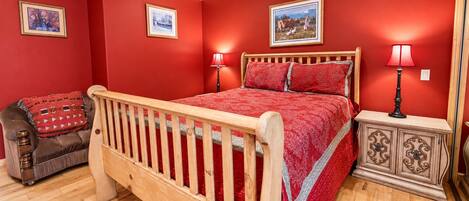 Un dormitorio con cama de madera, paredes rojas y ventilador de techo.