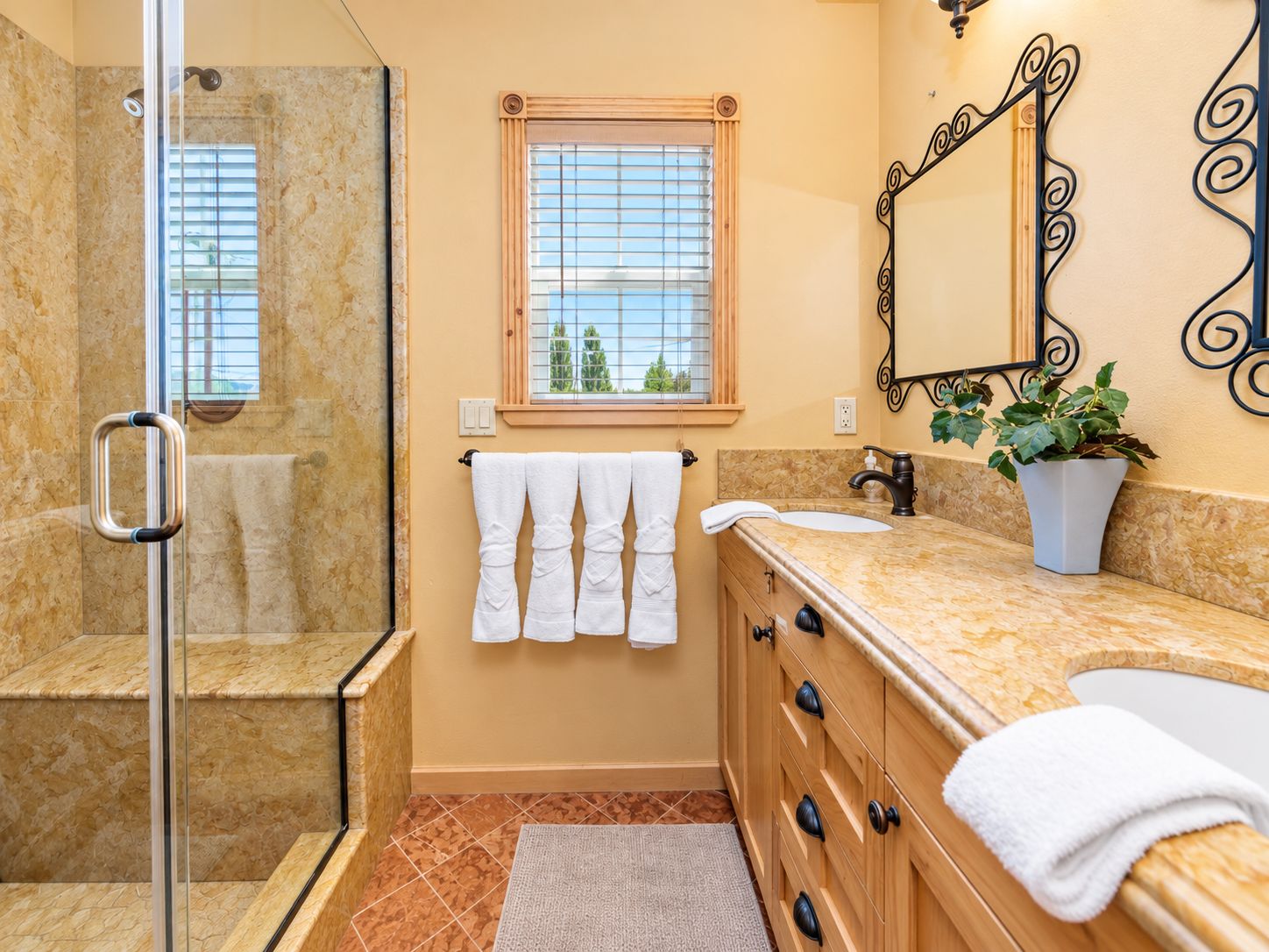 A bathroom with a glass shower enclosure, a vanity with a sink, a mirror, and a potted plant.