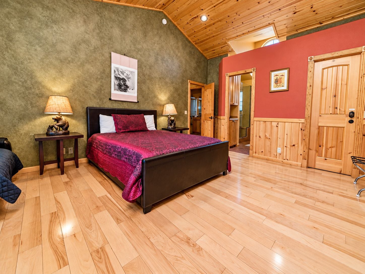 A bedroom with a bed, two bedside tables with lamps, a wooden ceiling, and a door.
