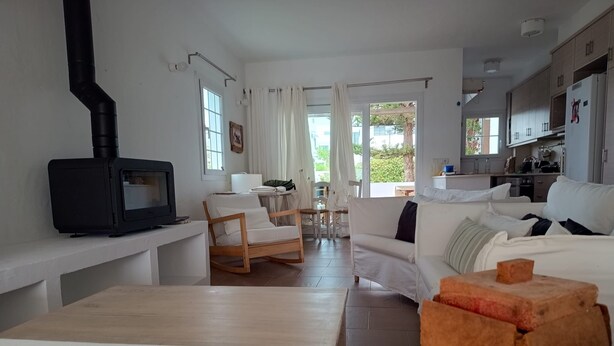 A modern living room with a fireplace, white sofas, a wooden coffee table, and a kitchen area in the background. - Fabulous 170 m² terraced house in the heart of Fornells, with pool and garden (Fornells)