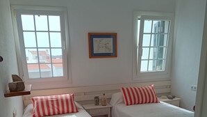 A room with two single beds, a small table, a shelf with decorative items, and a framed map on the wall. - Fabulous 170 m² terraced house in the heart of Fornells, with pool and garden (Fornells)