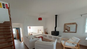 A spacious living room with a fireplace, white sofas, a wooden rocking chair, and a staircase. - Fabulous 170 m² terraced house in the heart of Fornells, with pool and garden (Fornells)