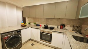 A compact kitchen with a washing machine, oven, and a coffee maker. - Penta Square - Luxury Studio Suite (Lahore)
