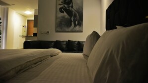 A hotel room with a bed, a black leather sofa, and a painting of a horse on the wall. - Penta Square - Luxury Studio Suite (Lahore)