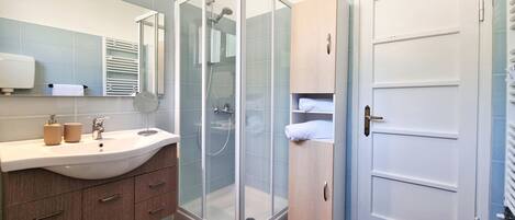 Un baño moderno con ducha de vidrio, lavamanos con artículos de aseo y espejo.