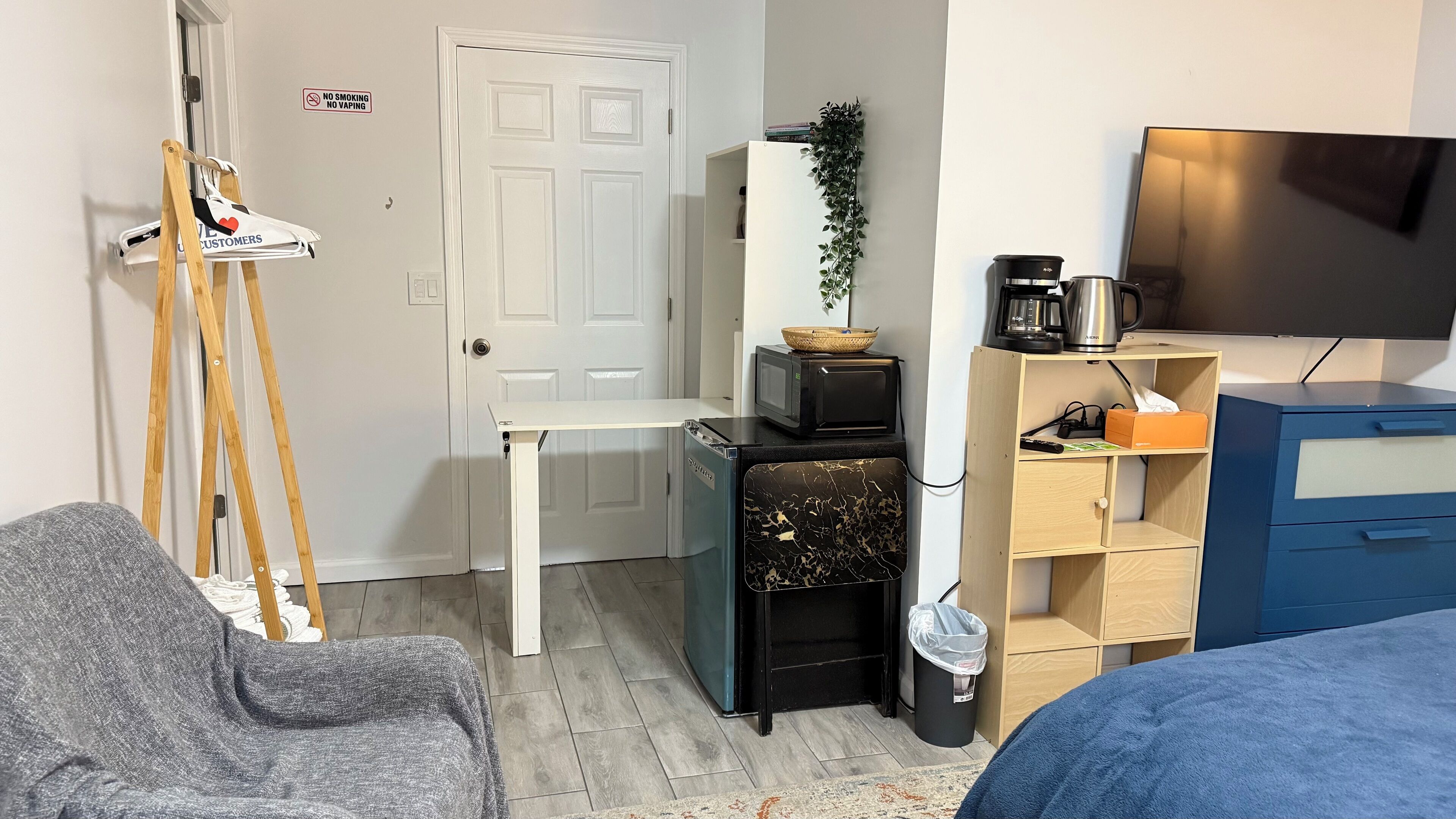 A compact living space with a kitchenette, a small dining table, a sofa, a TV, and a trash bin.