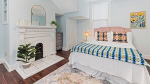 Quarto com lareira, cama com colcha colorida, ventilador de teto e janela com persianas.