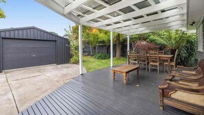 Een overdekt terras buiten met een houten vloer, een tafel en rieten meubels.