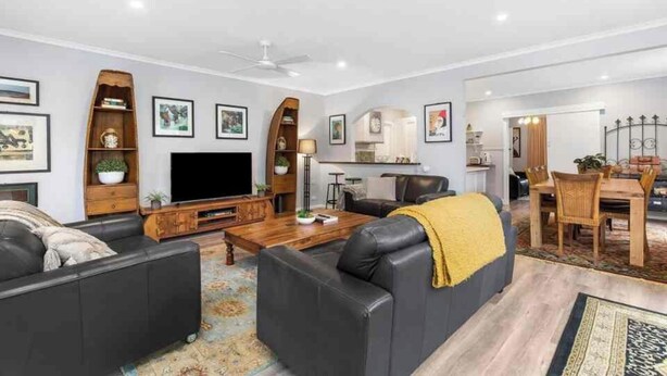 Een moderne woonkamer met een flatscreen televisie, zwarte leren banken, een houten salontafel en een eethoek met een houten tafel en stoelen.