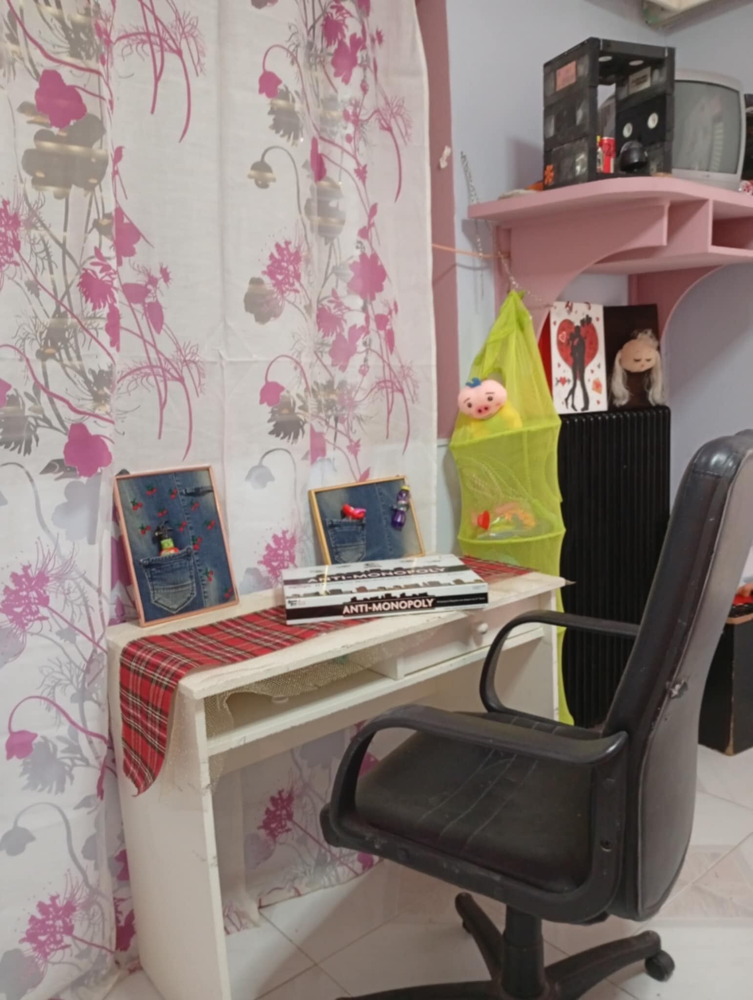 A workspace with a desk, two framed pictures, a chair, and a shelf with various items.