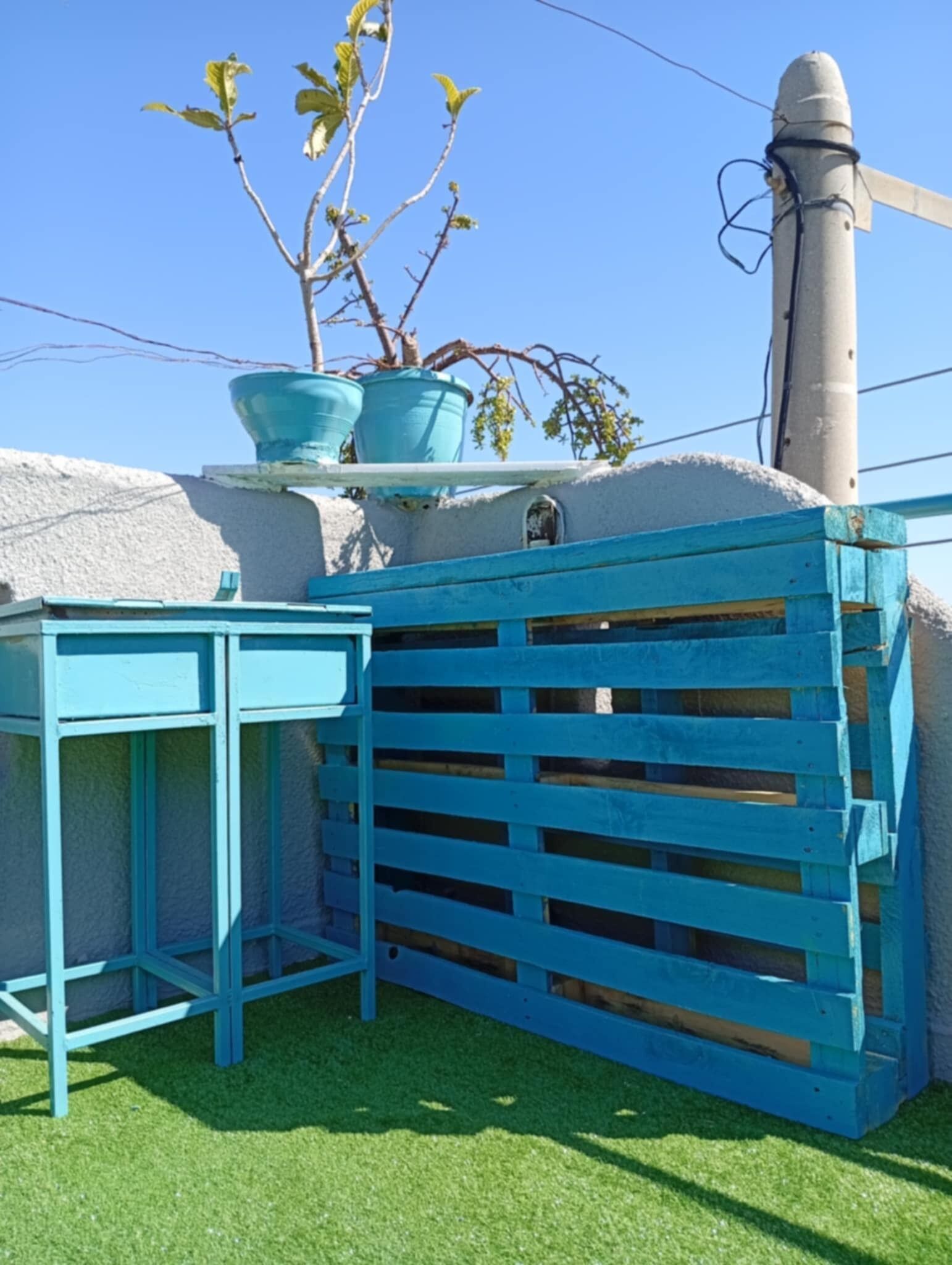 Une clôture en bois bleue, un pot de fleurs et un mur blanc avec une fenêtre.