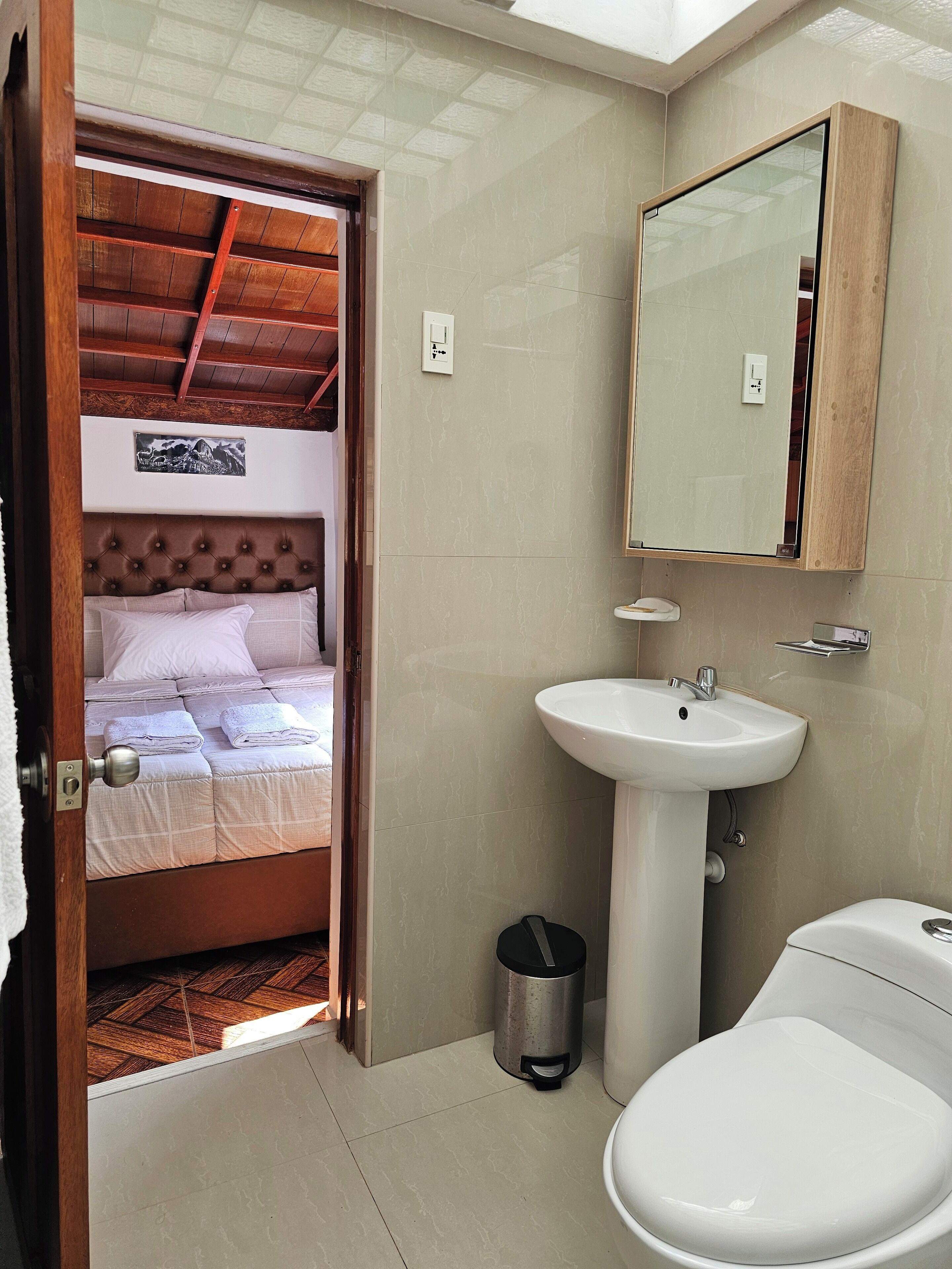 A bedroom with a bed, a bedside table, a wall-mounted mirror, a sink, and a toilet.