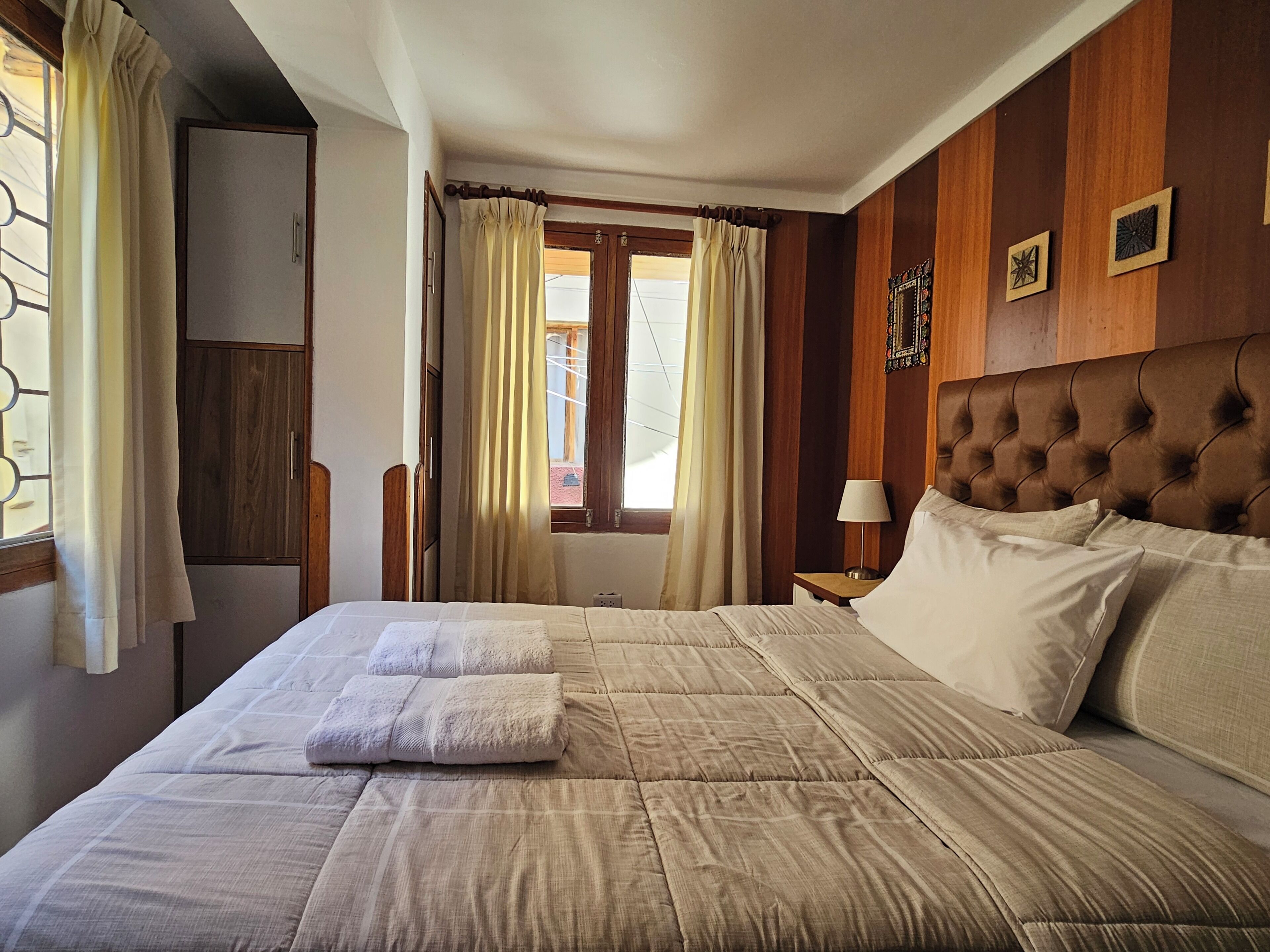 A hotel room with a large bed, wooden headboard, and a window with curtains.