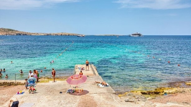 A coastal scene with clear blue waters, a pier, and a cruise ship in the distance. - The Apateu (San Pawl il-Baħar)