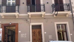 A two-story building with a balcony on the second floor, a wooden door, and two cars parked in front. - Fata34  (Reggio Calabria)