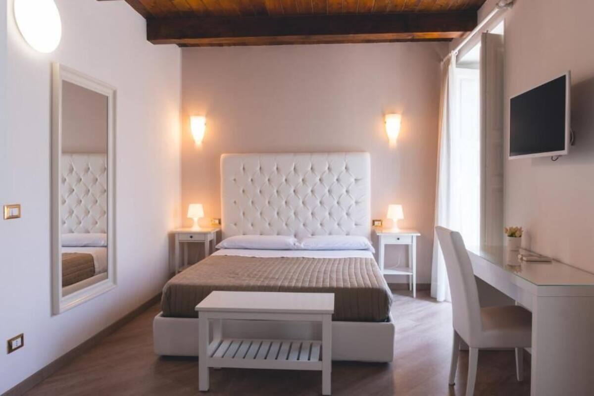 Un dormitorio con cabecera capitonada, lámparas de noche, un escritorio con silla y un televisor montado en la pared.