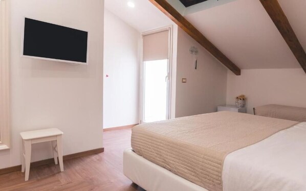 Une chambre à coucher comprenant un lit, une petite table de chevet, un téléviseur fixé au mur et une porte donnant sur une autre pièce.