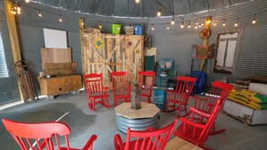 Un intérieur rustique avec des chaises rouges disposées autour d’une table en bois centrale, le tout agrémenté de divers objets en bois et en métal.