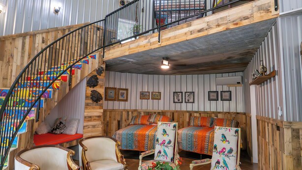 Un vaste espace de vie de style loft, doté d’un escalier à volutes, de murs en bois et d’un espace aménagé en mezzanine pour le lit.