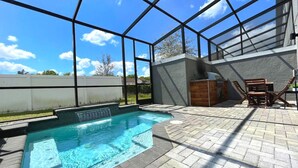 Una piscina con cascada, rodeada por un patio amoblado con mobiliario exterior y una parrilla.