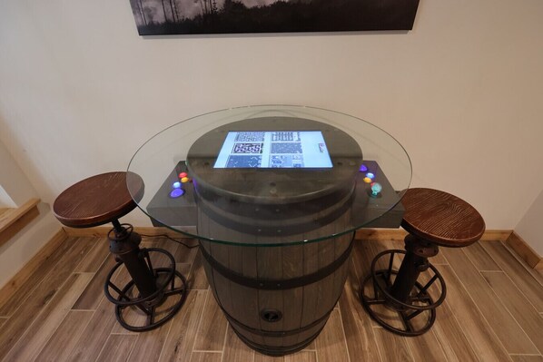 Een ronde glazen tafel met een houten tonvoet, twee krukken en een digitaal scherm.