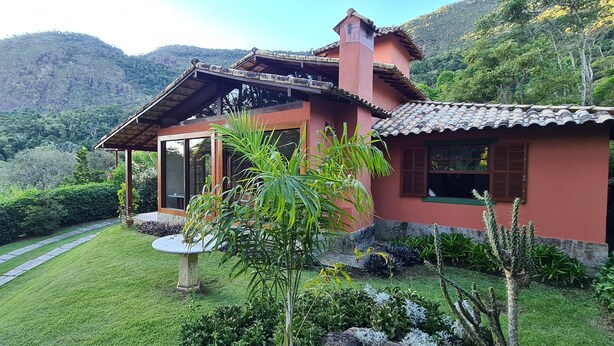 A house with a red exterior, a tiled roof, and a garden with various plants and a stone pathway. - Country House with Pool and Cinematic View in Luxury Condominium (Pedro do Rio)