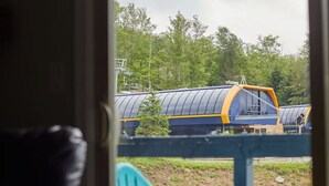 Blick von einem Zimmer mit einer Tür, die nach draußen führt. Vor der Tür steht ein blauer Adirondack-Stuhl, und ein Zug mit blau-gelben Waggons fährt auf Gleisen vorbei.