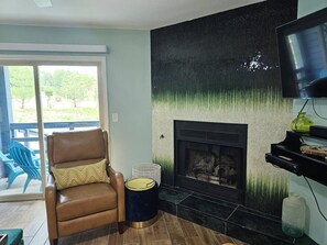 Ein Wohnzimmer mit Kamin, Ledersessel, Fernseher und Blick ins Freie.