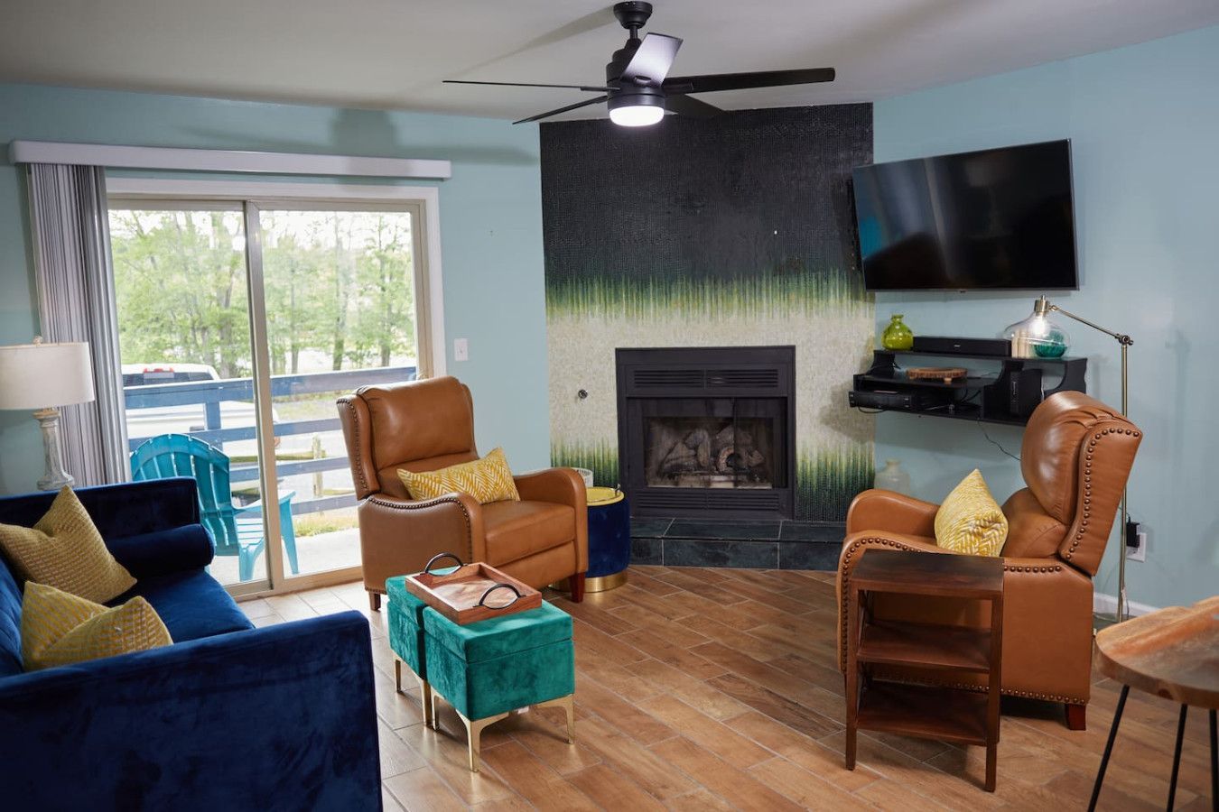 A living room with a fireplace, leather armchairs, a blue sofa, and a television mounted on the wall.